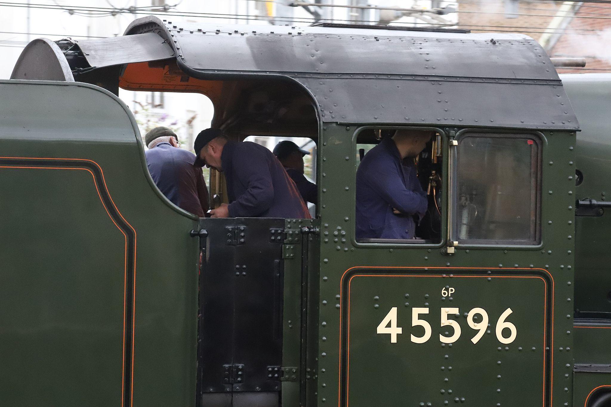 Footplate crew. LMS Jubilee class steam locomotive 45596 "Bahamas" in BR livery passing Royal Oak London Underground railway station at 07:05 on 22-Jul-2022 hauling The Railway Touring Company's "West Somerset Steam Express" to Minehead.