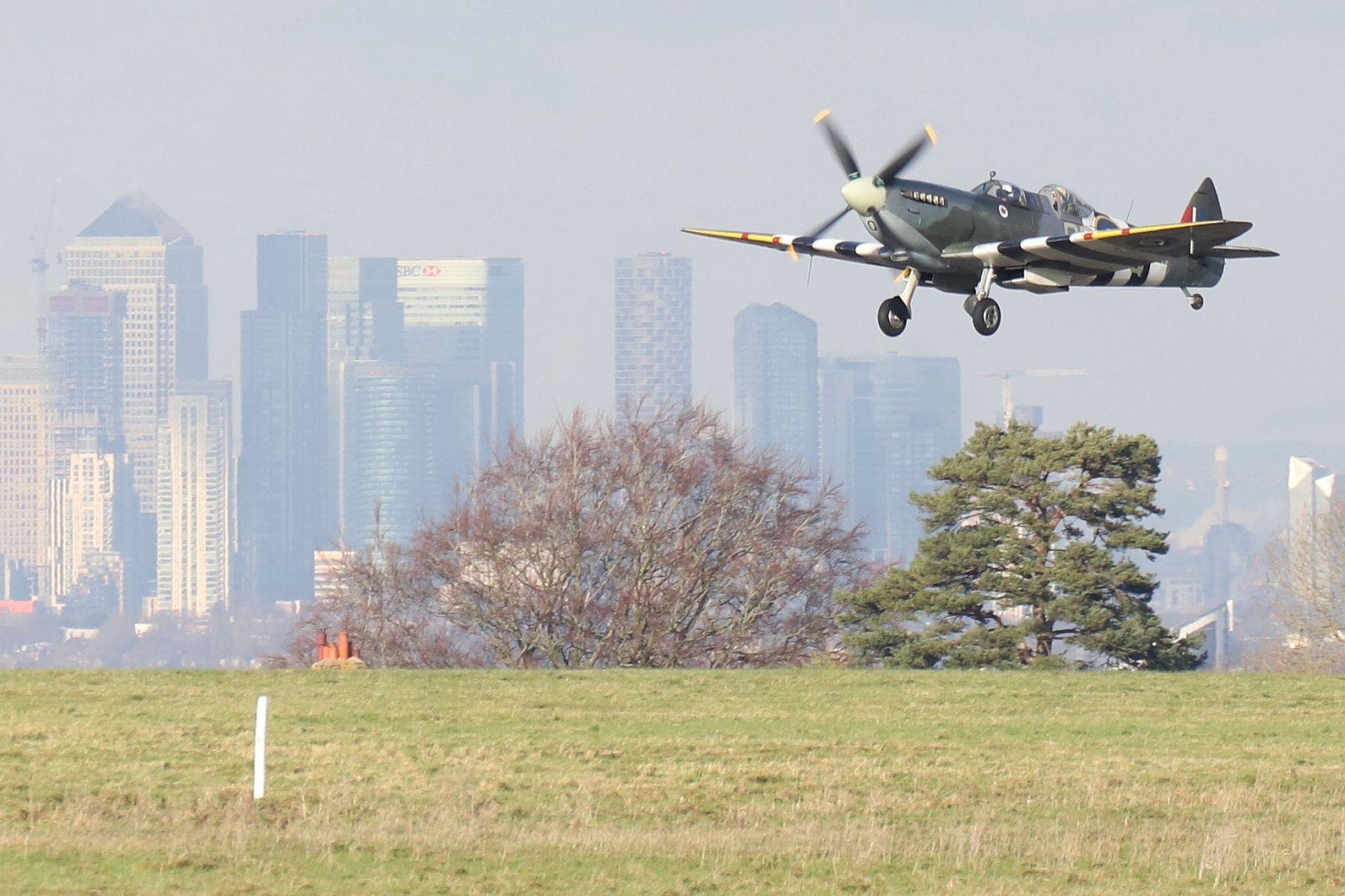 Spitfire taking off from the former RAF Biggin Hill with Canary Wharf in the background. Biggin Hill Spitfire Factory two seat Spitfire T.9 MJ627.