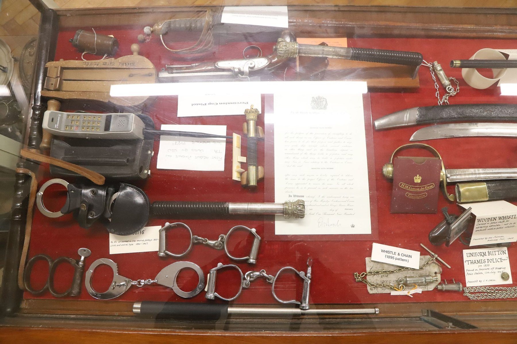 Various handcuffs, a 1980s mobile phone and a wooden rattle for summoning help. Metropolitan Police Marine Policing Unit Museum, River Thames, London.