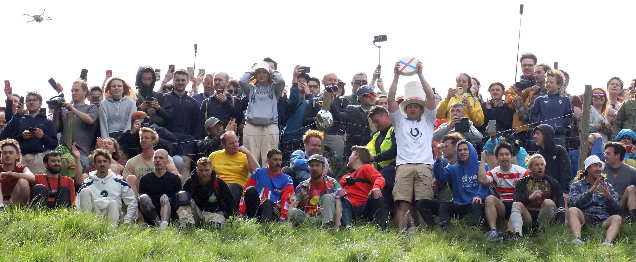The Master of Ceremonies raises a wheel of cheese above his head before starting the race. Coopers Hill Cheese Rolling Race. 29-May-2023. Race downhill. Gloucestershire tradition.