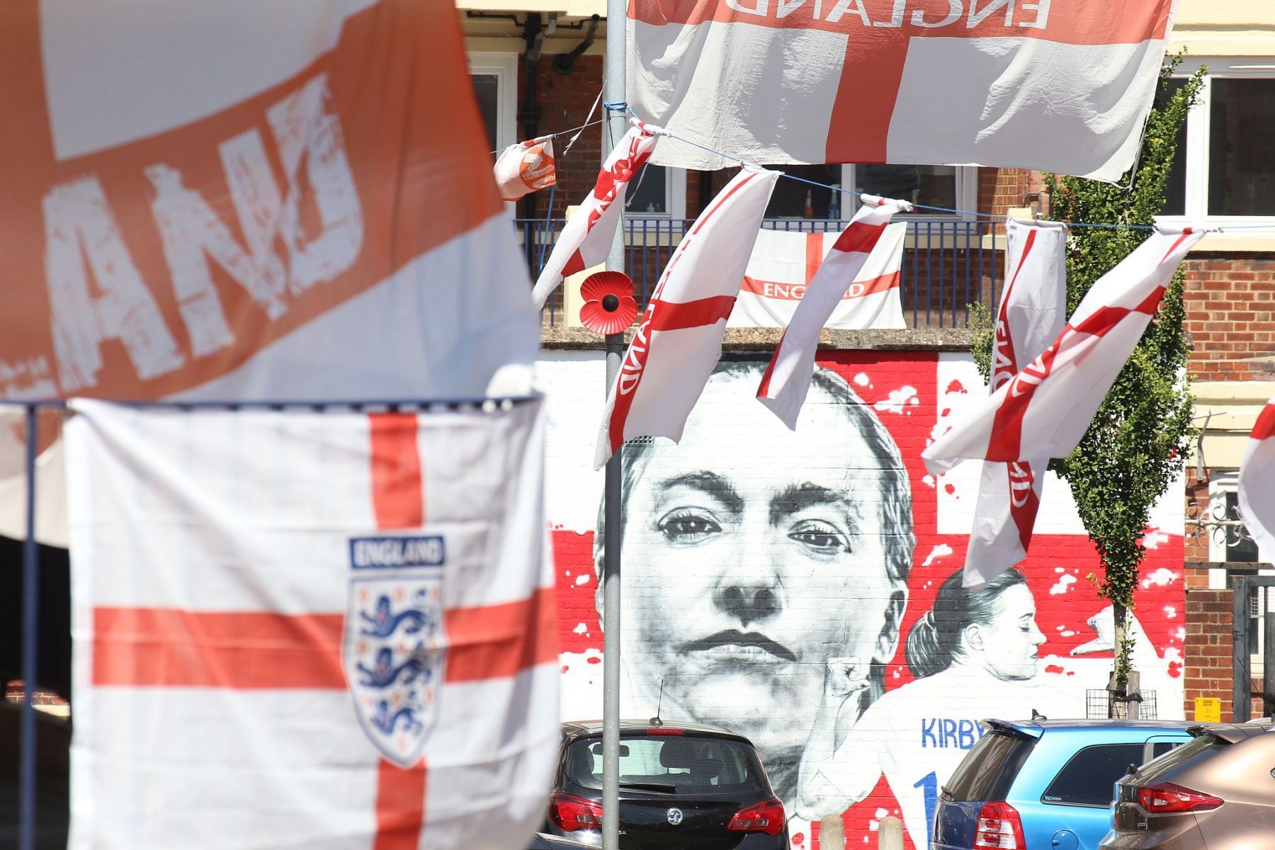 Spray painted mural of footballer Fran Kirby at the Kirby Estate (Bermondsey SE London) seen through England flags flying from the flat's balconies