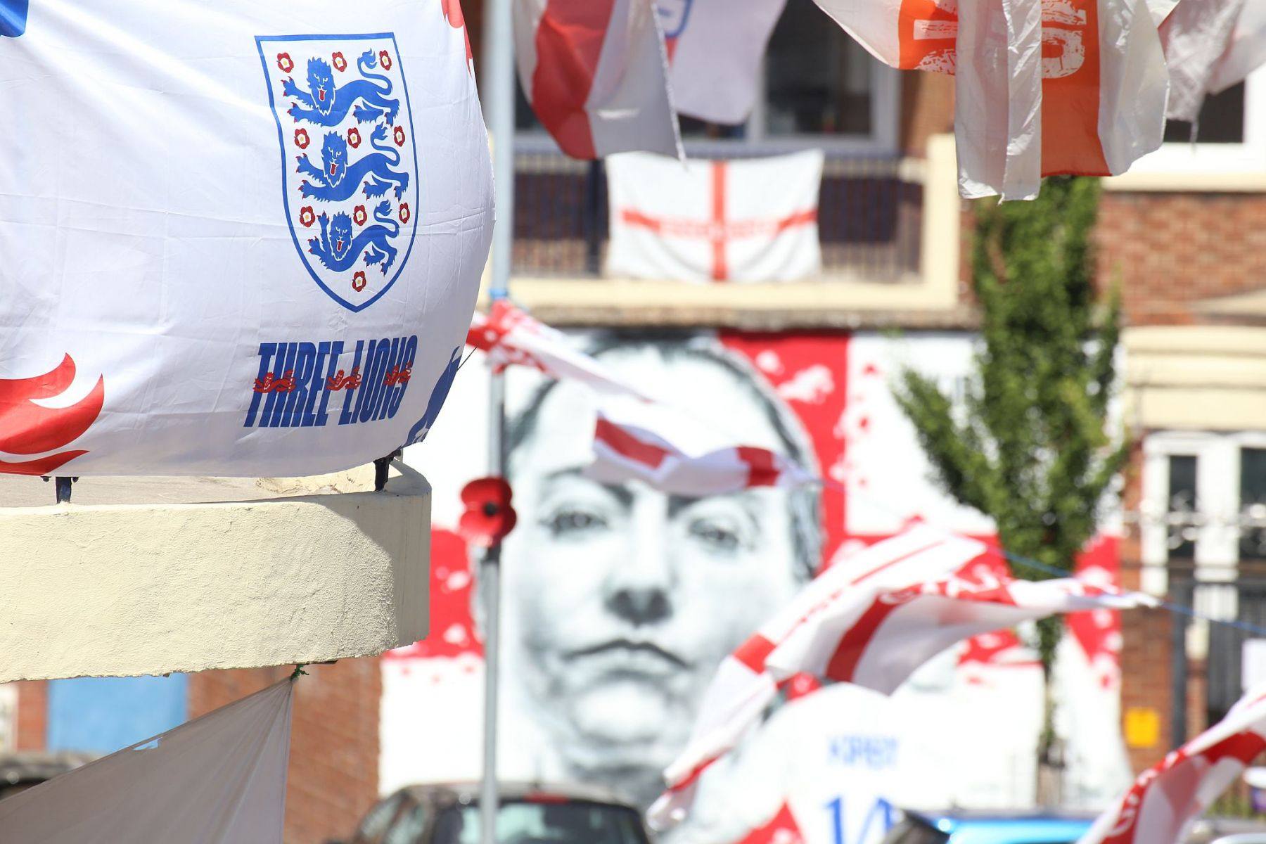Spray painted mural of footballer Fran Kirby at the Kirby Estate (Bermondsey SE London) seen through England flags flying from the flat's balconies