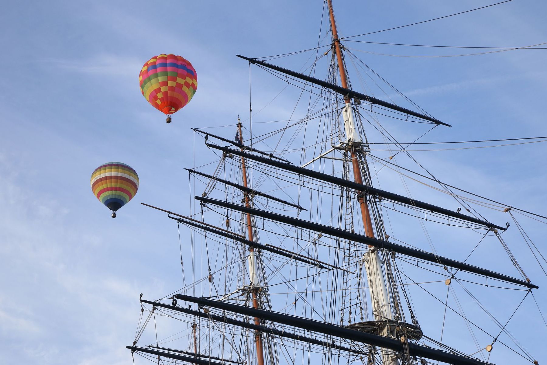 A flight of 46 hot air balloons taking part in the 2019 Lord Mayor’s Balloon Regatta fly over Greenwich passing the Cutty Sark ship and Old Royal Navy College by the River Thames early on the morning of  09-Jun-2019. City of London.