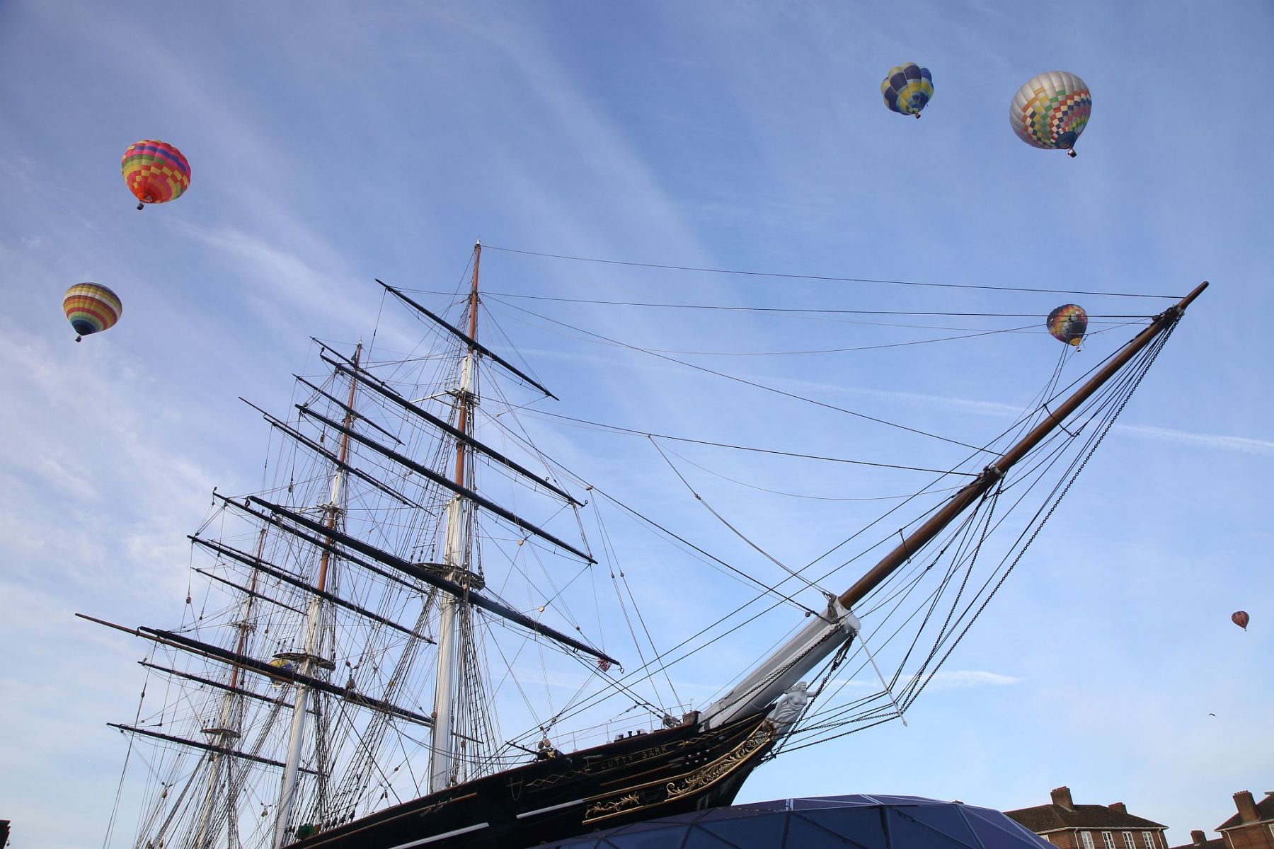 A flight of 46 hot air balloons taking part in the 2019 Lord Mayor’s Balloon Regatta fly over Greenwich passing the Cutty Sark ship and Old Royal Navy College by the River Thames early on the morning of  09-Jun-2019. City of London.