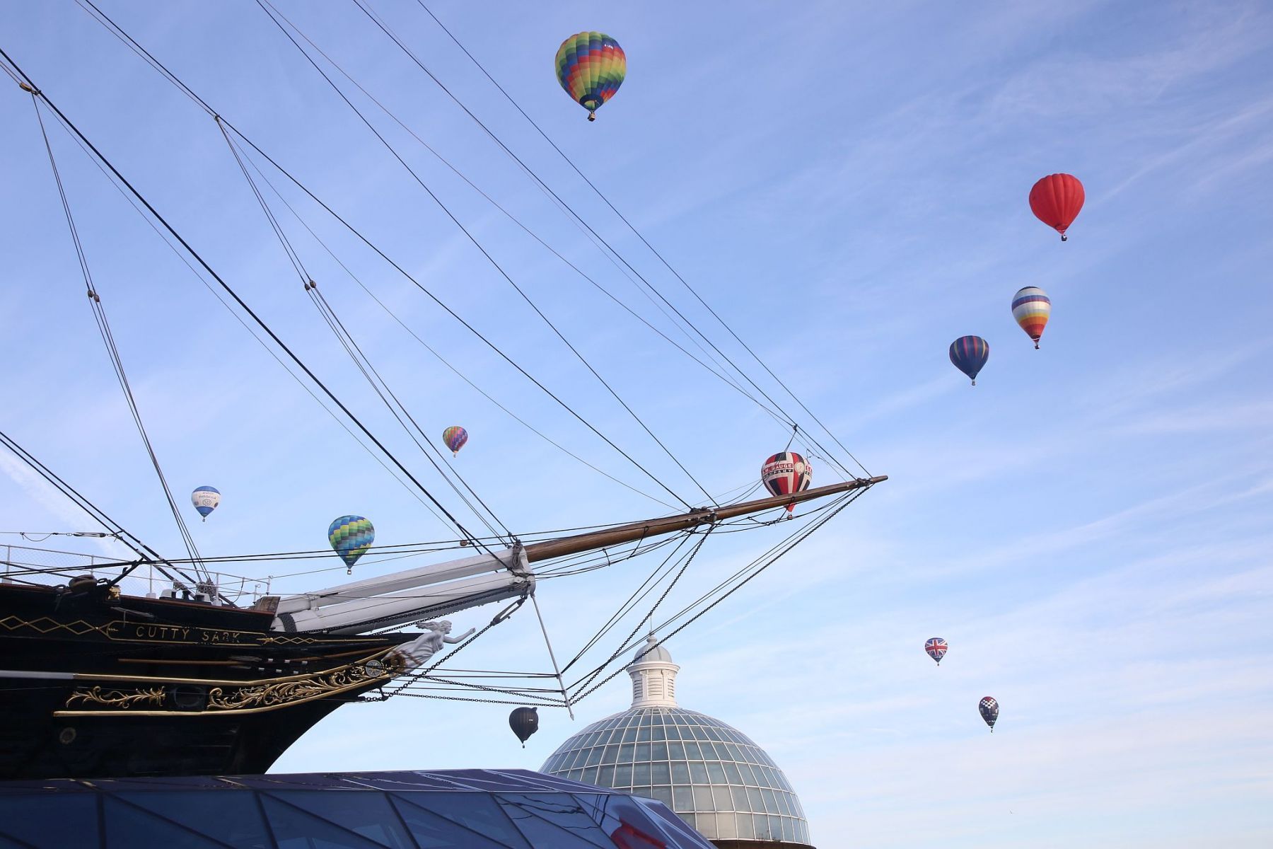 A flight of 46 hot air balloons taking part in the 2019 Lord Mayor’s Balloon Regatta fly over Greenwich passing the Cutty Sark ship and Old Royal Navy College by the River Thames early on the morning of  09-Jun-2019. City of London.
