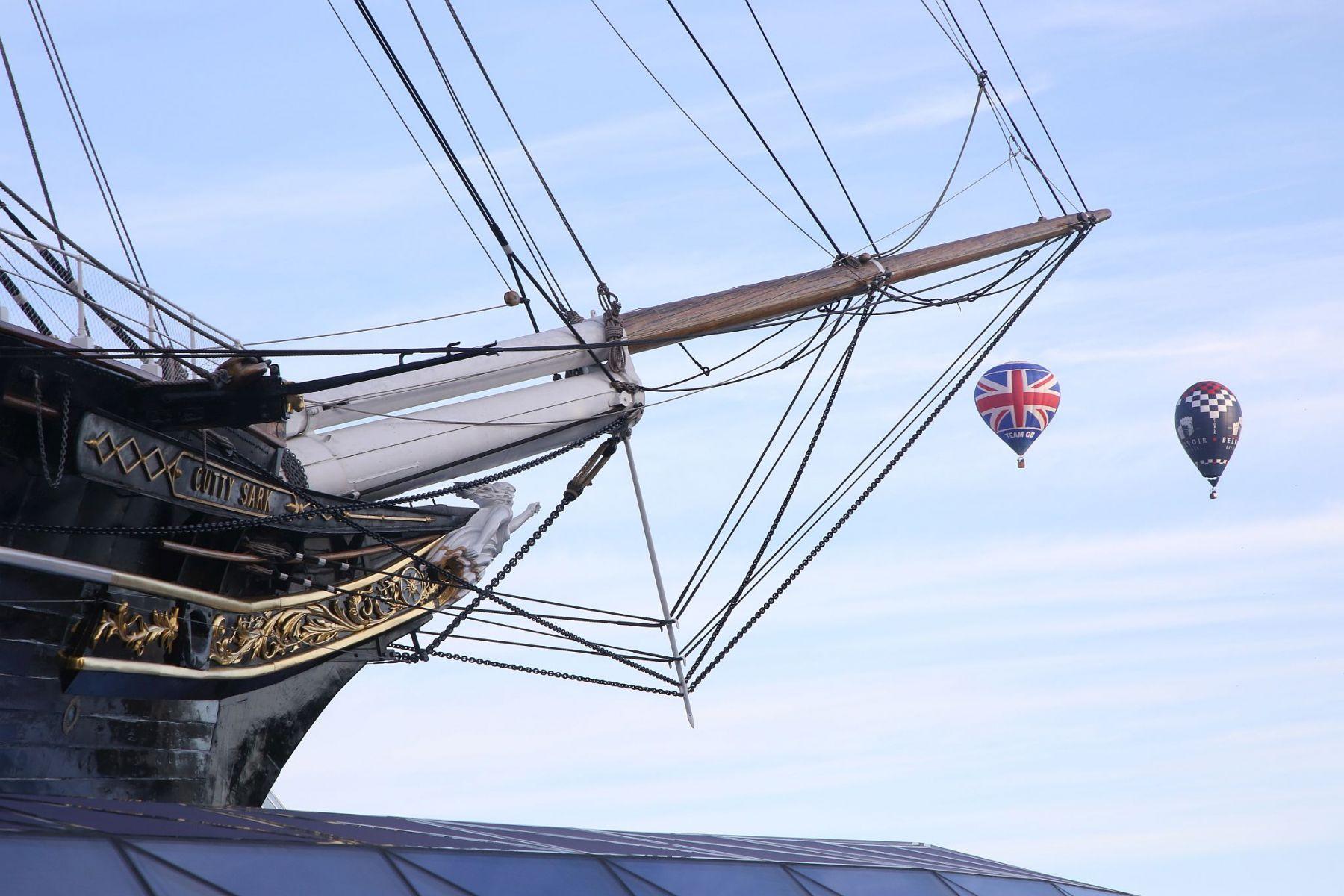 A flight of 46 hot air balloons taking part in the 2019 Lord Mayor’s Balloon Regatta fly over Greenwich passing the Cutty Sark ship and Old Royal Navy College by the River Thames early on the morning of  09-Jun-2019. City of London.