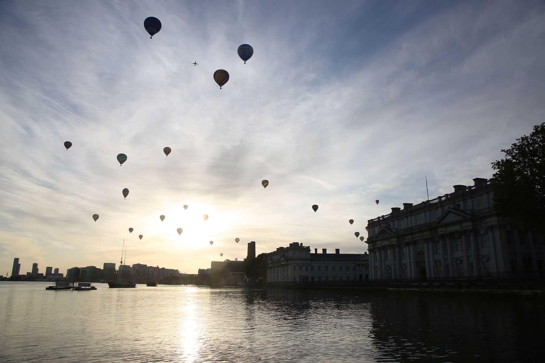 A flight of 46 hot air balloons taking part in the 2019 Lord Mayor’s Balloon Regatta fly over Greenwich passing the Cutty Sark ship and Old Royal Navy College by the River Thames early on the morning of  09-Jun-2019. City of London.