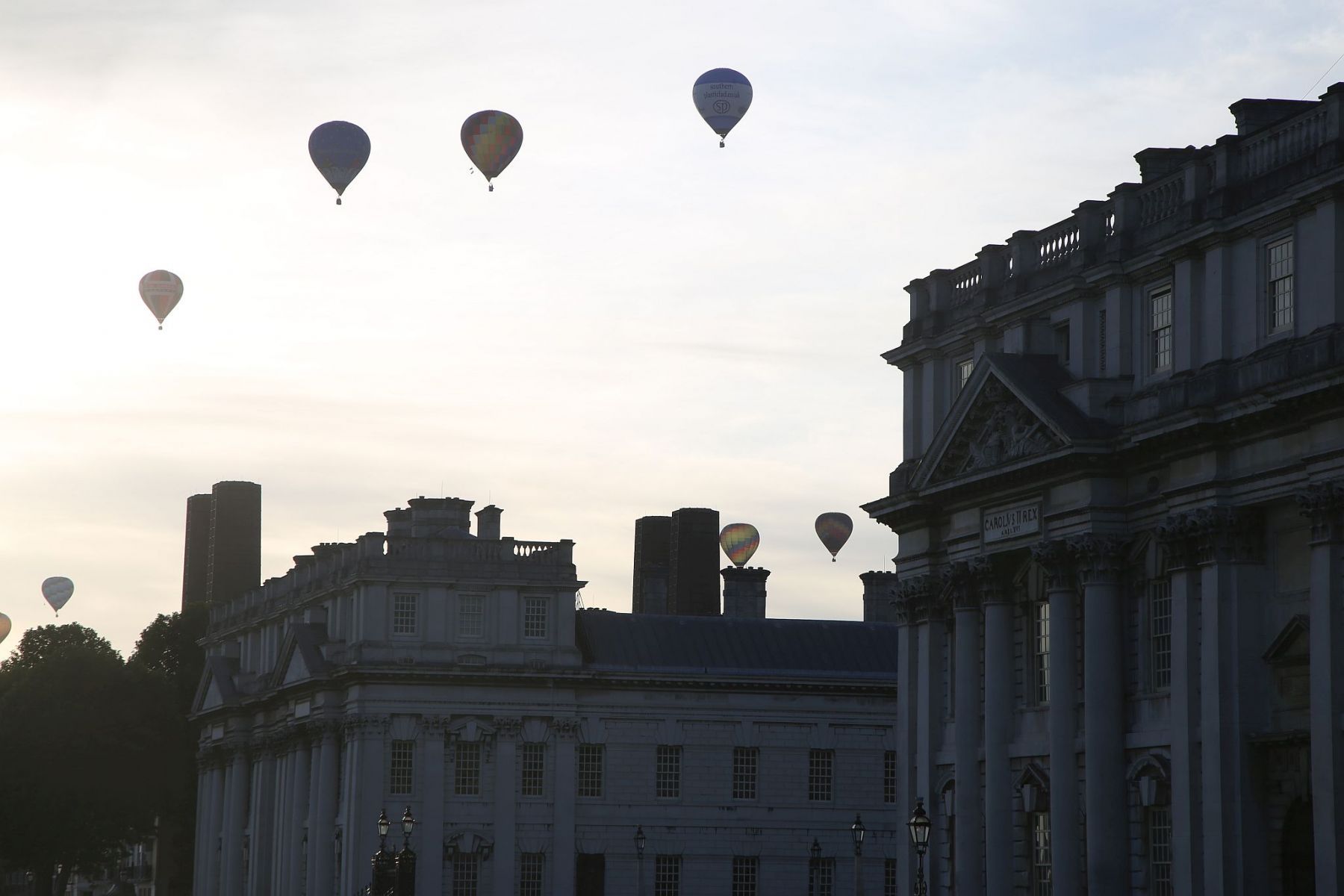 A flight of 46 hot air balloons taking part in the 2019 Lord Mayor’s Balloon Regatta fly over Greenwich passing the Cutty Sark ship and Old Royal Navy College by the River Thames early on the morning of  09-Jun-2019. City of London.