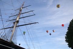 A flight of 46 hot air balloons taking part in the 2019 Lord Mayor’s Balloon Regatta fly over Greenwich passing the Cutty Sark ship and Old Royal Navy College by the River Thames early on the morning of  09-Jun-2019. City of London.