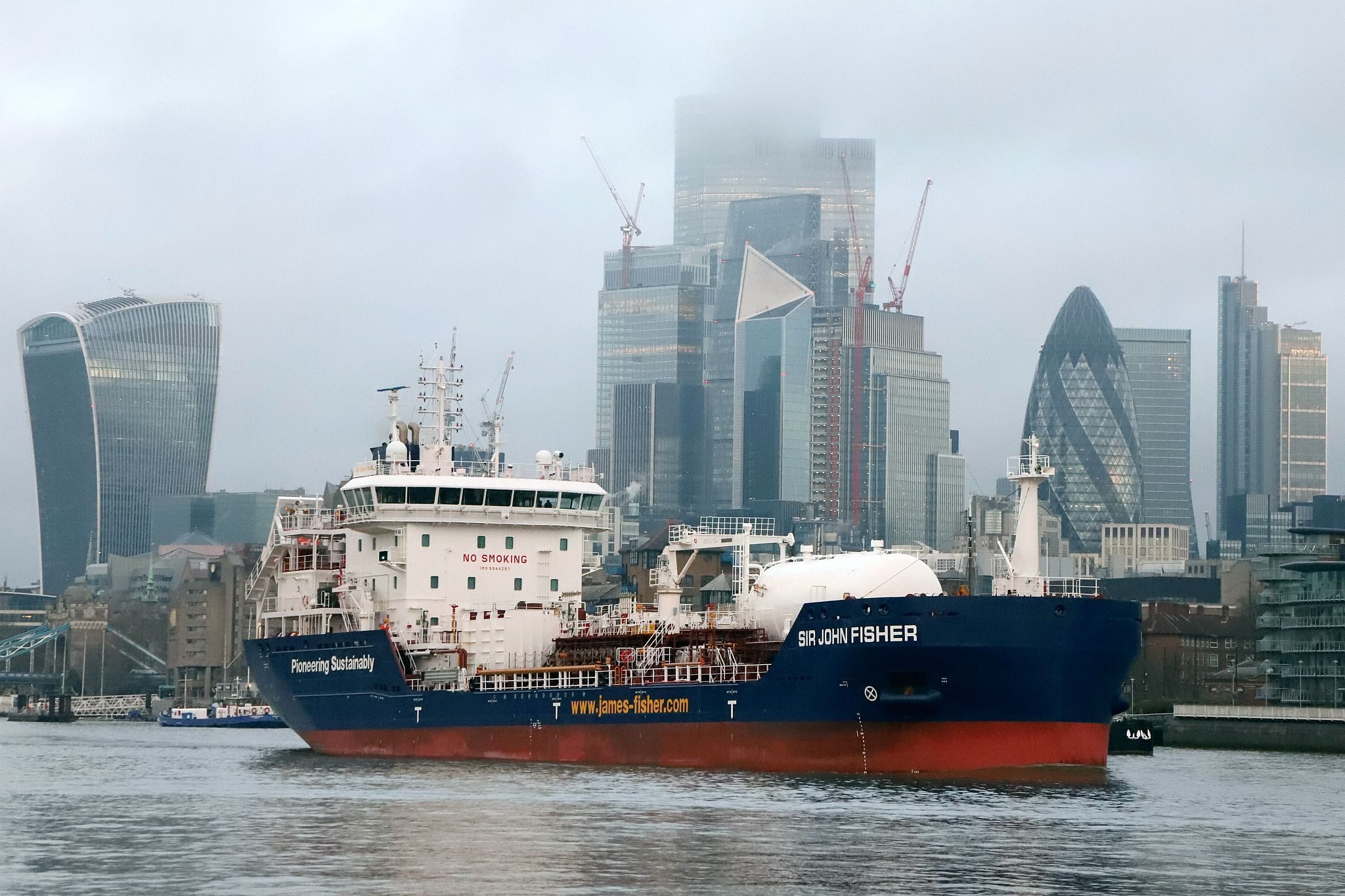 Chemical Tanker “Sir John Fisher”, owned by James Fisher, leaves central London on 29-Mar-2023 and passes downstream on the River Thames with the City of London in the background.