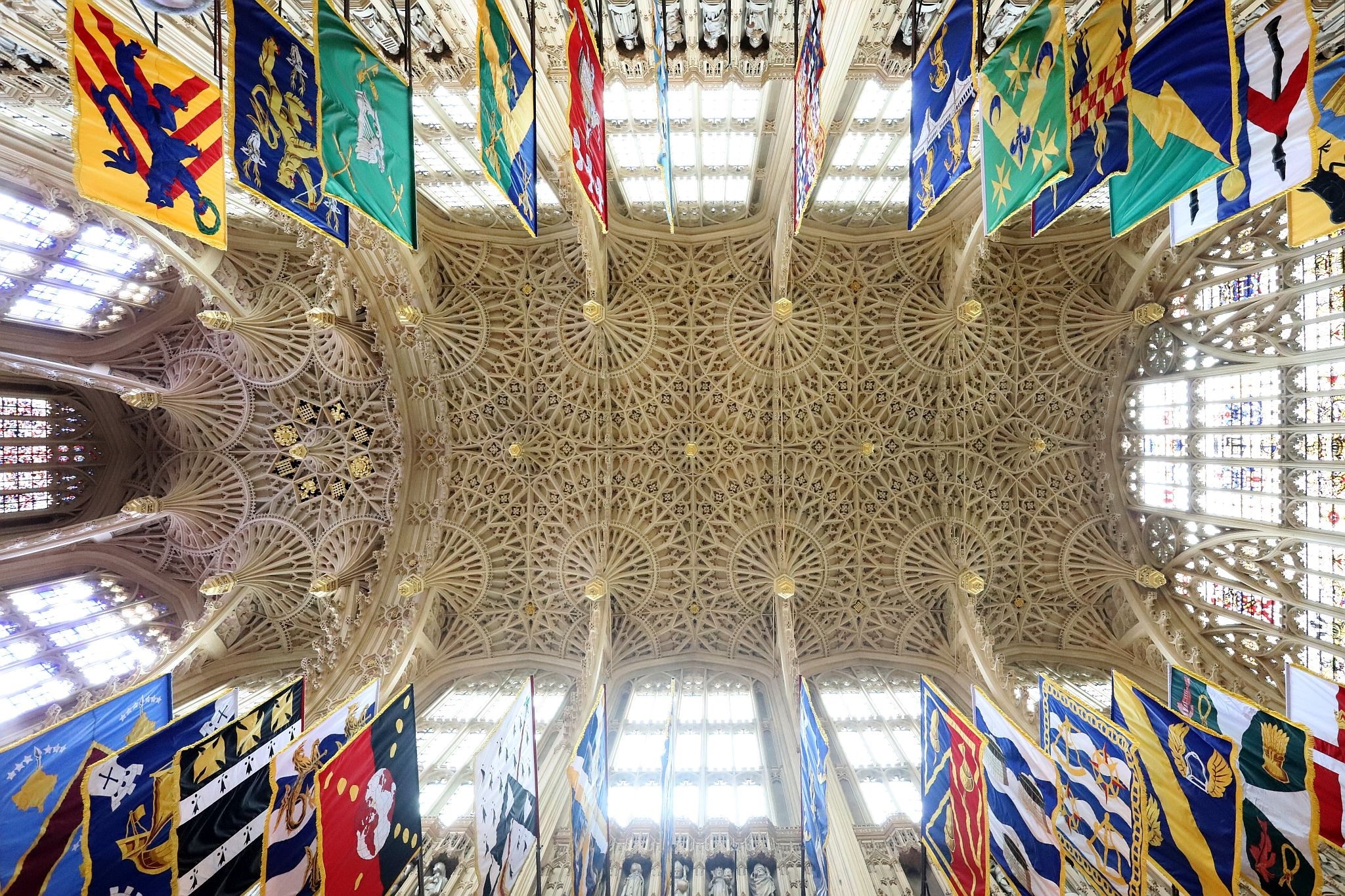The roof of the Lady Chapel at the Eastern end of Westminster Abbey, overlooking the Houses of Parliament. The beautiful fan vaulted ceiling is framed by the colourful flags. Picture taken 13-May-2023. Ceiling.